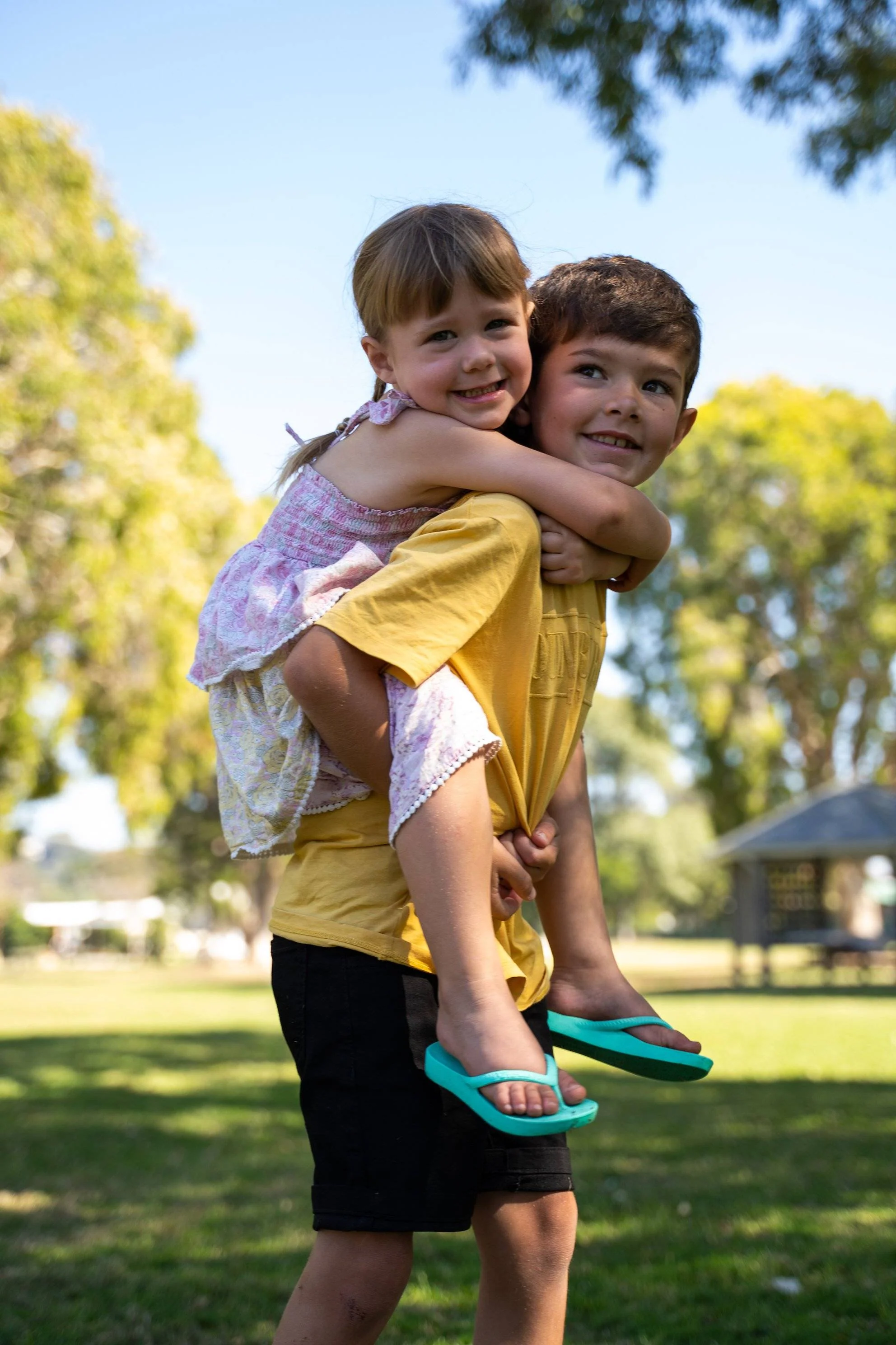 Archies arch support kids thongs in a mint green style pictured being worn by a young girl being carried on a young boy's back