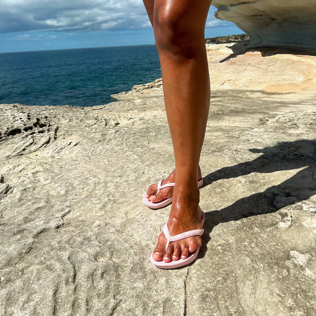 Archies arch support thongs in a pink style pictured being worn by a woman standing by the ocean