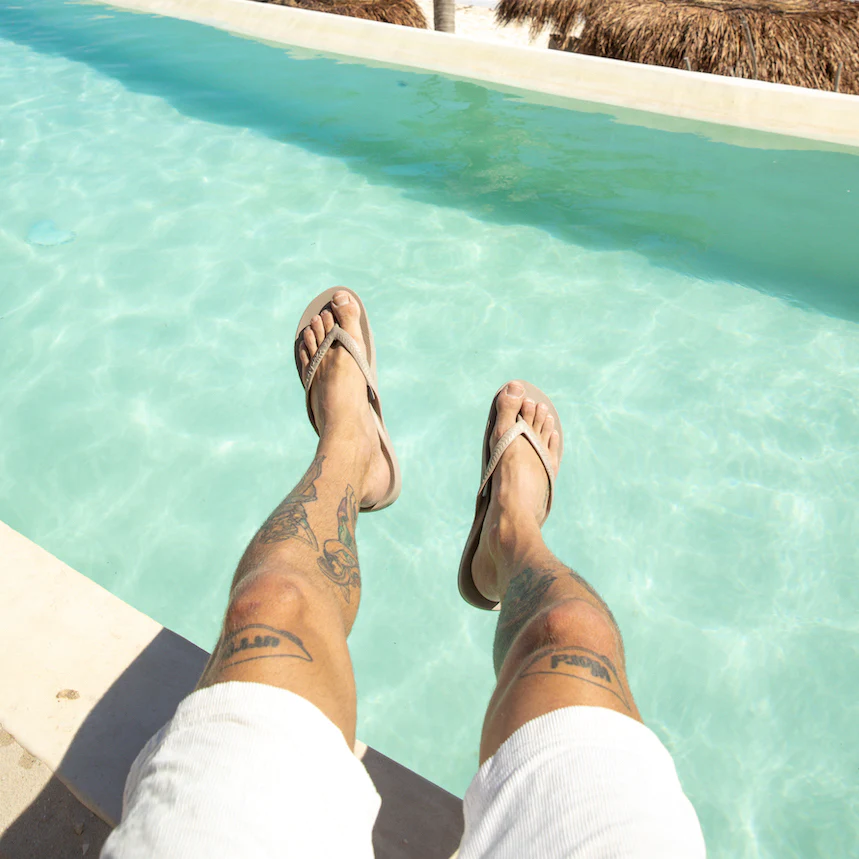 Archies arch support thongs in a taupe style pictured being worn by a man with his legs danging over a pool