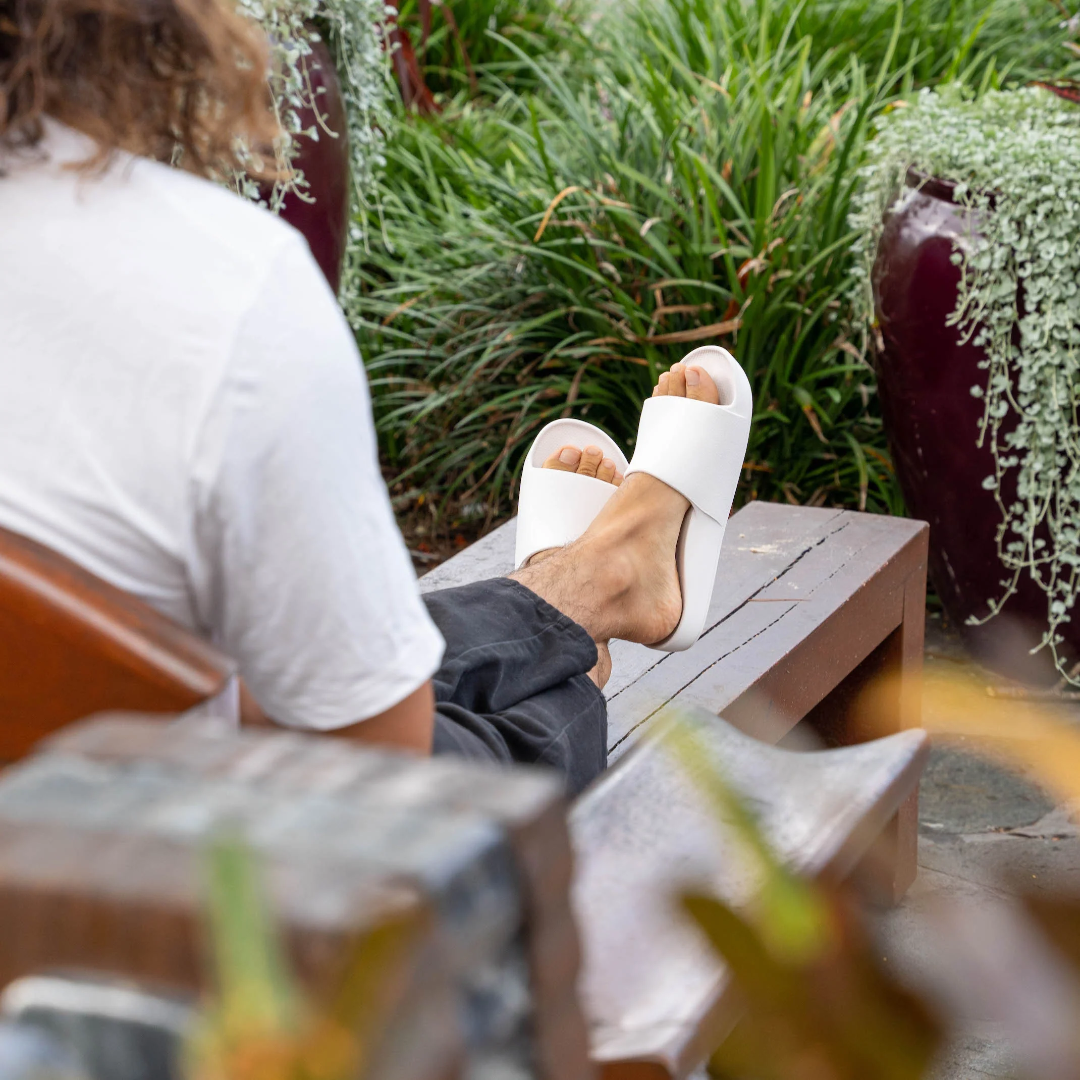 Archies arch support slides in a white style pictured being worn by a  man with his feet up on a bench